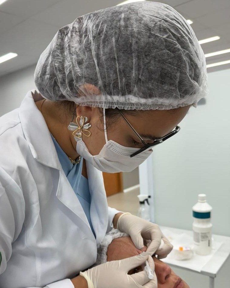 Rayla Barone, de jaleco, touca e luvas, durante um atendimento